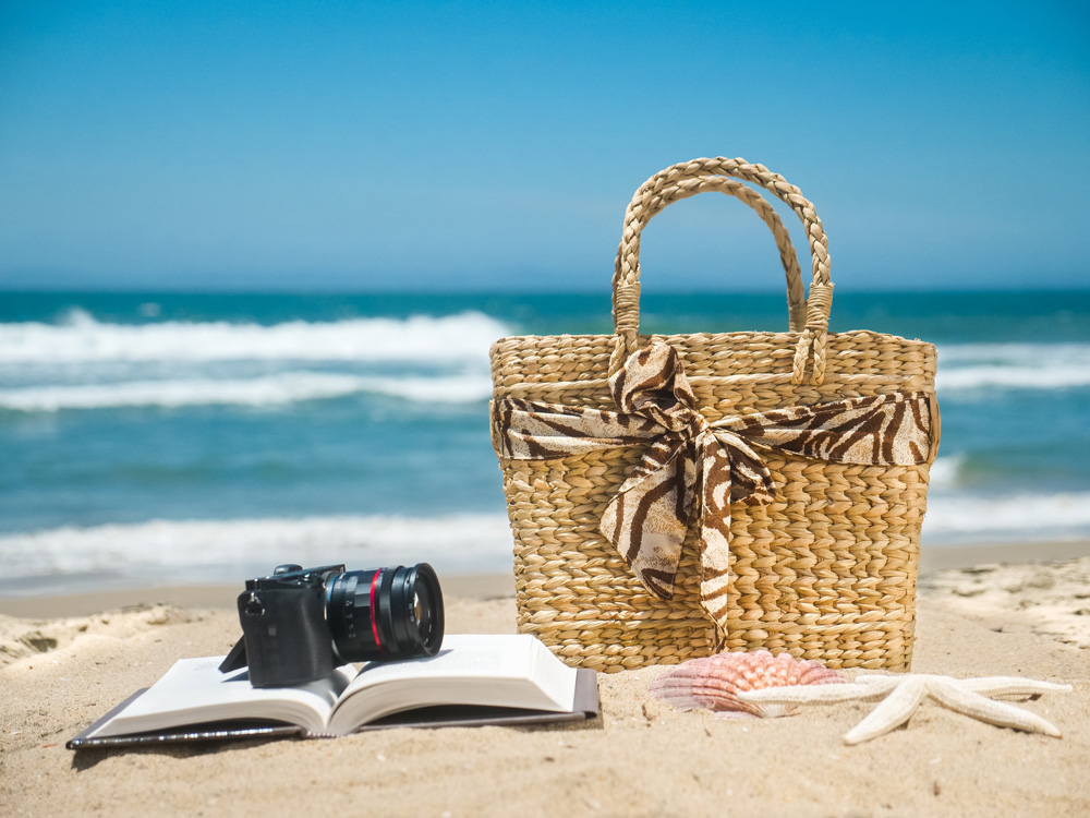 Sahilde deniz manzarasına karşı bir kitap, kamera ve sahil çantasının fotoğrafı