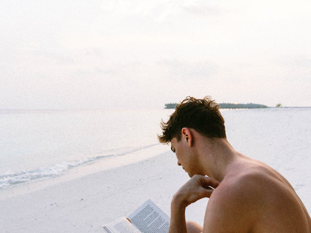 Denize karşı bir adam kendisine kalabalıktan uzak sessiz bir köşe bulmuş kitabını okuyor