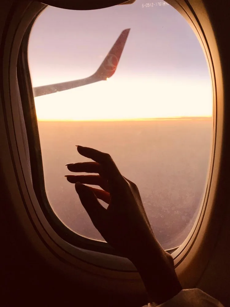 Uçak camından elini uzatan yolcu ve gün batımı