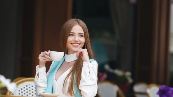 Beyaz gömlekli ve güzel kadın kahve fincanını elinde tutuyor