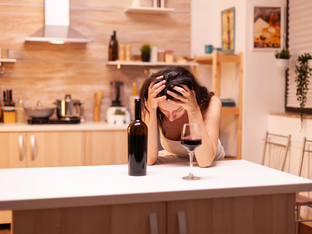 Tatilde fazla alkol tüketmekten depresyon içine girmiş bir kız masada kafasını tutuyor
