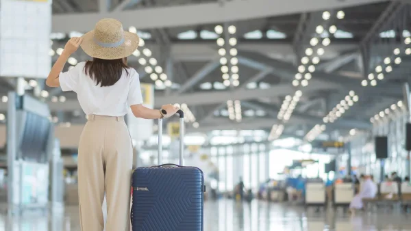 Havaalanında elinde valiziyle etrafa bakan arkası dönük bir kadın