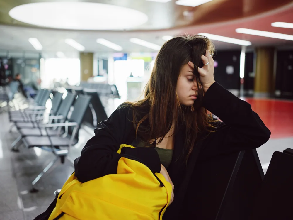 havaalanında bir kadın jet lag yaşadığı için koltuklarda oturarak başını tutuyor