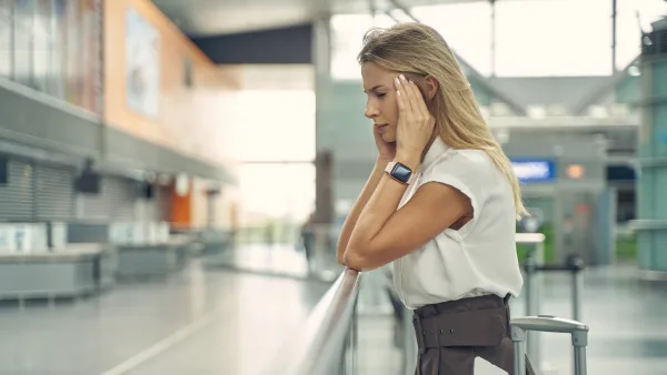 havaalanında uzun seyahatler sonucu baş ağrısı çeken kadın kendine gelmek için uğraşıyor