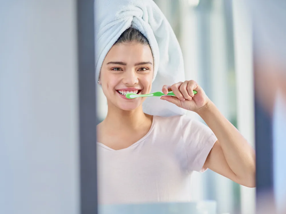 Evde diş beyazlatma yöntemlerinden olan doğal diş macununu hazırlayan kadın ayna karşısında dişlerini fırçalıyor
