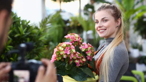 çiçekçi kadın ellerindeki çiçeklerle kameraya poz veriyor