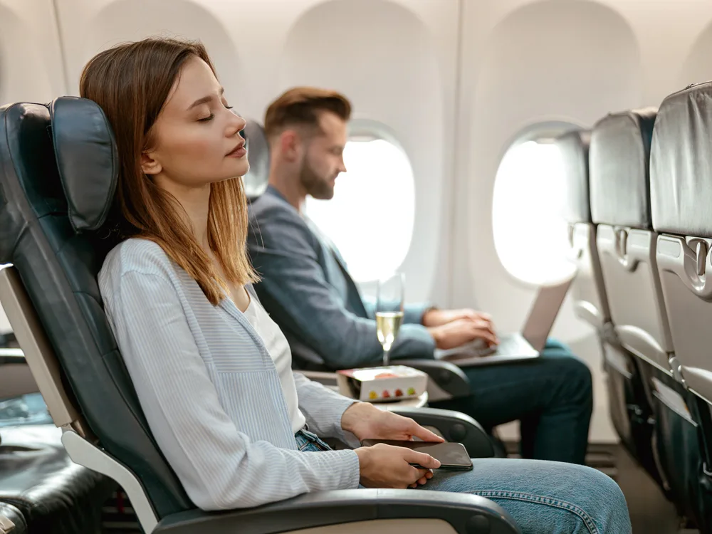 uçak koltuğunda oturarak gözlerini dinlendiren kadın ve yan koltuğunda şampanya içen adam