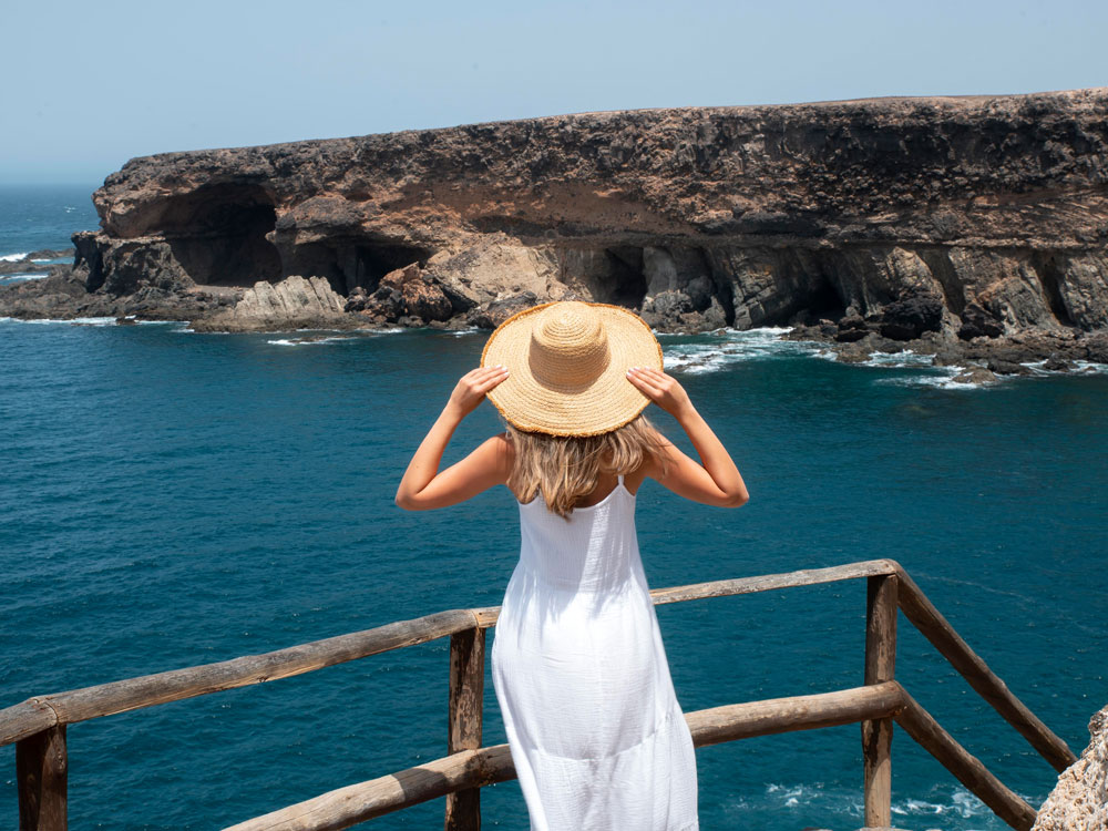 Beyaz elbise ve şapka giymiş bir kadın, iyi bir destinasyonda denize doğru bakıyor.