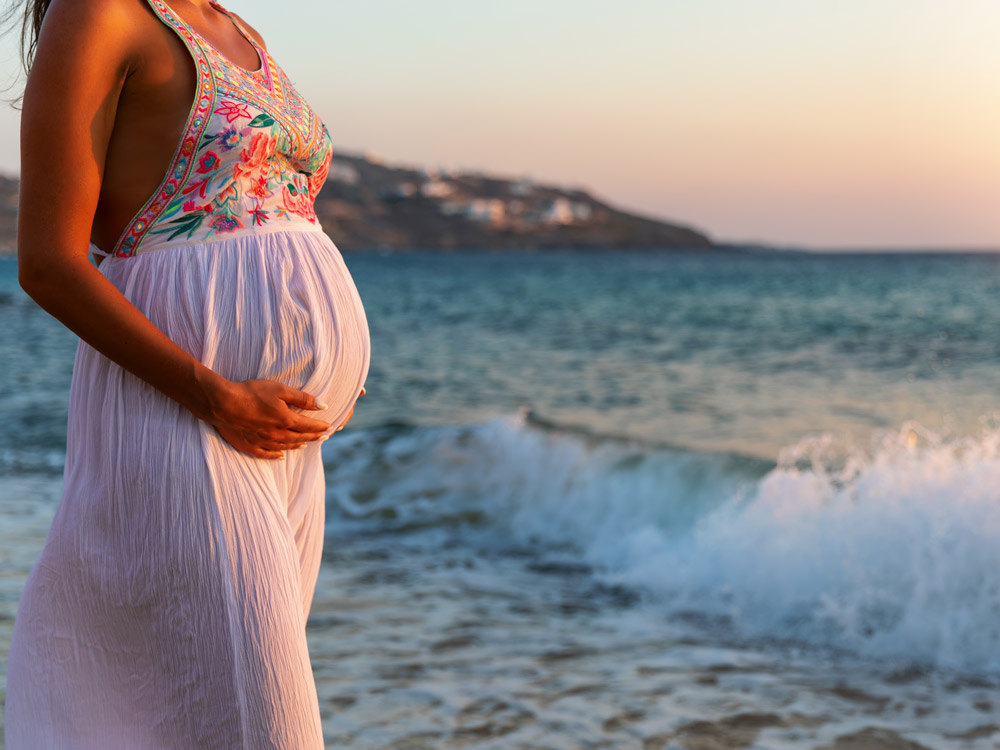 Hamilelikte plaj tatili yapan kadın gün batımını izliyor.